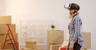 Oldukça Kafkas kadın bir yeni düz günde hareketli bir Vr kulaklık yaparken kutuları ile bir oturma odası etrafa bakıyor. İçinde