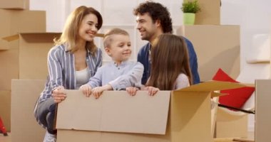 Gülümseyen ve onların başparmak gösterilmesini çocuklar arasında kutuları, birlikte oturan mutlu iyi görünümlü anne. Kutuya oturan çocuklar. Gün içinde hareket. İçinde