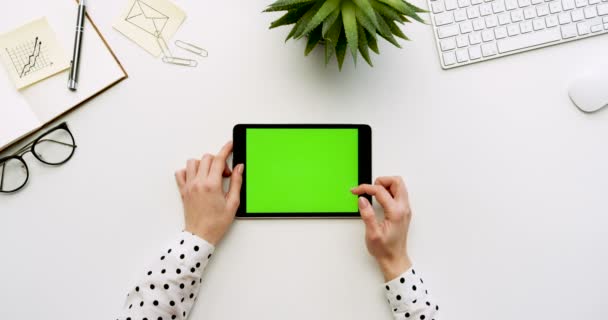 ホワイト オフィスの机と緑色の画面と女性の手がそれをテーピングで黒いタブレット コンピューターの平面図です。水平。事務所の横にあるもの。クロマ キー. — ストック動画