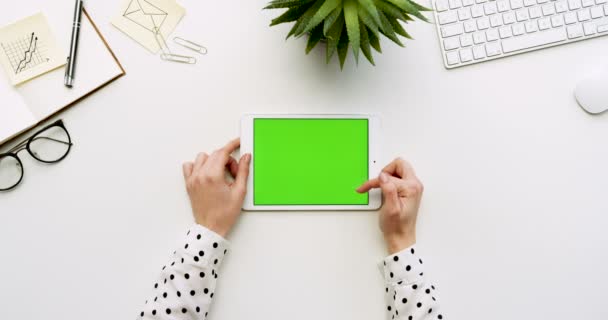 Vista dall'alto sulla scrivania bianca dell'ufficio e sul tablet bianco con schermo verde e con le mani femminili attaccate su di esso. Orizzontale. Roba da ufficio. Chiave cromatica . — Video Stock