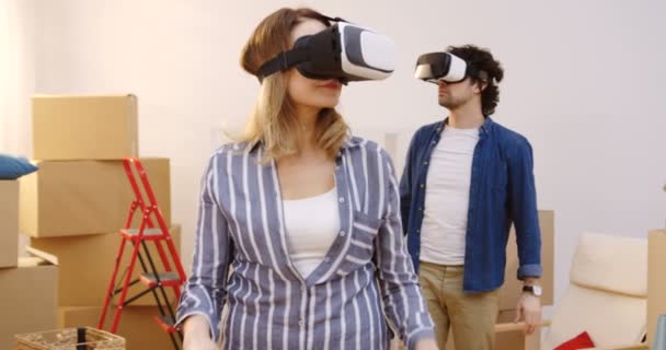 新しいアパートに移動しながらボックスいっぱいリビング ルームでカメラの前に立って Vr ガラスの結婚されていたカップルの肖像画のショット。屋内 — ストック動画