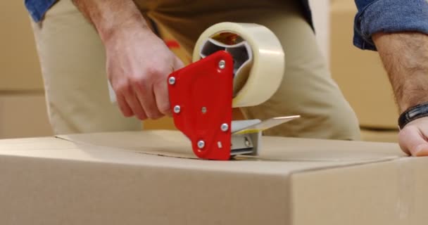 Close up of the mans hands packing a carton box with a sticky tape. Indoors — Stock Video