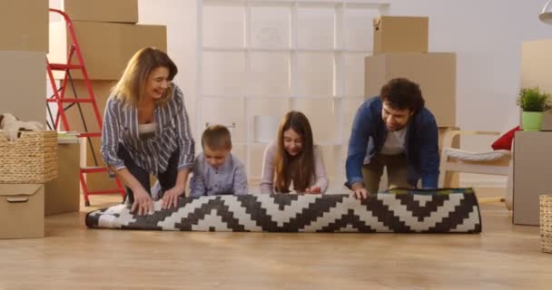 Wesoły kaukaskiej rodziny rozpakowaniu Wzorzysty dywan w przytulny pokój pełen z pól podczas ich przenoszenia w nowym mieszkaniu. Wewnątrz — Wideo stockowe