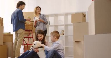 Mutlu çocuk ve ebeveynleri kutuları arka planda açmak iken katta bir labrador köpekle oynayan kız. İnç yeni ev taşıma. Kapalı