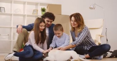 Yeni dairende hareket ederken açmak kutuları ve ev şeyler çevrili yerde otururken bir sevimli köpek okşayarak neşeli mutlu aile portre vurdu. İçinde