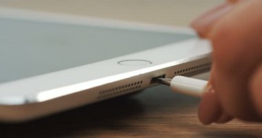 Ahşap masa ve içinde attınız şarj yatan gümüş tablet cihazın makro çekim. Yakın çekim