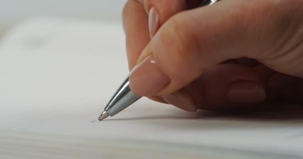Närbild av kvinnlig hand skriva med en penna ett ord som ekonomiska i anteckningsboken på den tomma sidan. Makro — Stockvideo