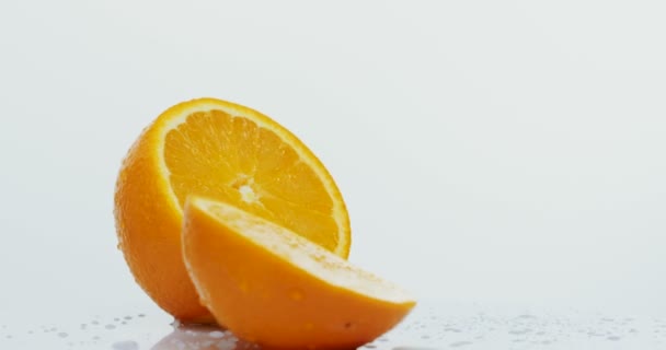Disparo macro de las dos mitades de naranja con gotas de agua rodando sobre el fondo blanco de la pared. De cerca. — Vídeos de Stock