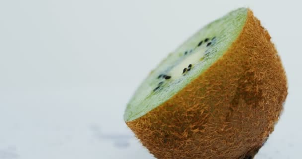 Macro van de helft van de kiwi met water druppels op de witte muur achtergrond rollen. Close-up — Stockvideo