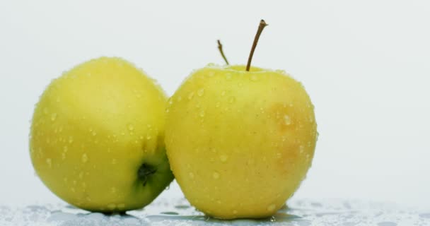 Macro tiro de três maçãs amarelas com gotas de água rolando sobre o fundo da parede branca. Fechar — Vídeo de Stock