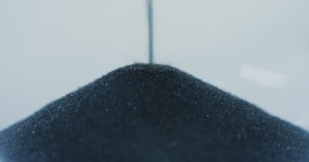Macro prise de vue du sable noir sirotant par le haut sur le dessus à l'intérieur de l'horloge de sable. Gros plan — Video