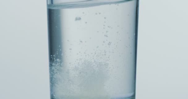 Detailní záběr z tabletu klesá ve sklenici vody a syčí. Makro fotografování — Stock video