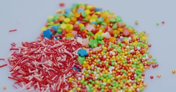 Primer plano de los pequeños caramelos de colores vidriosos de diferentes tipos que yacen sobre el fondo blanco. Macro — Vídeo de stock