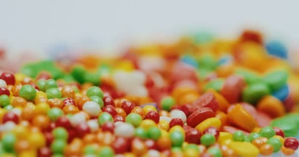 Macro shooting of the glazed little colourful candies of different shapes spinning in front of the camera on the white background. Close up — Stock Video