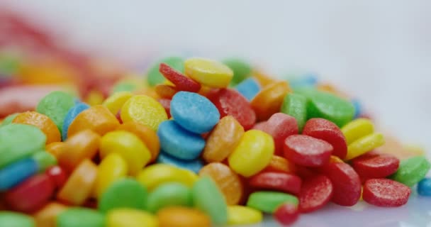 Närbild av glaserade små färgglada socker godis i olika former rullande framför kameran på den vita bakgrunden. Makrofotografering — Stockvideo