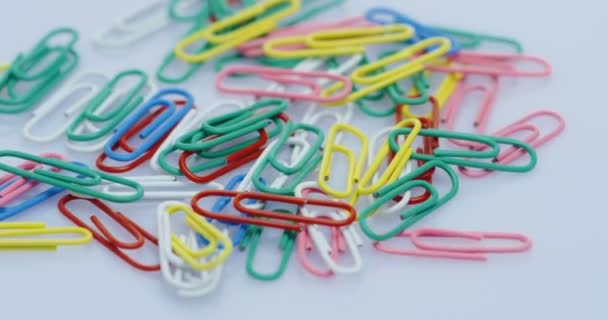 View from above on the spinning paper clips in colours lying on the white background. Close up — Stock Video