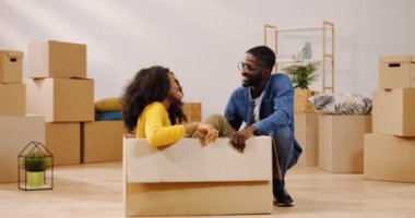 Rahat Oda kutuları arasında ortasında karton kutuda otururken, konuşurken ve sevgilisi ile gülüyor genç kıvırcık Afrikalı-Amerikalı kadın. Kapalı