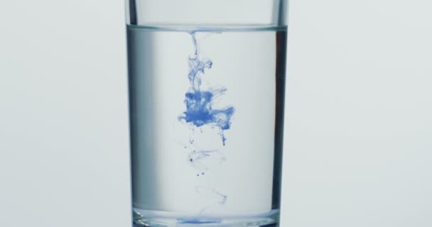 Tiro macro de la pintura azul derretiéndose en el vaso de agua. De cerca. — Vídeo de stock