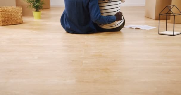 Traseira do casal afro-americano casado sentado no chão entre caixas e olhando para o plano plano plano, considerando um projeto para uma sua nova casa. Para dentro — Vídeo de Stock