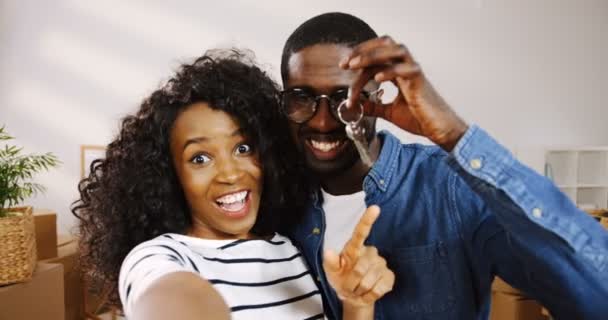 Портрет афроамериканской счастливой супружеской пары, снимающей видео-чат в гостиной и показывающей ключи от новой квартиры во время переезда. POV. Закрывай. В помещении — стоковое видео