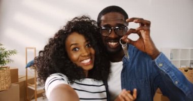 Afro-Amerikalı neşeli evli çiftin video şapka takıp, mutlu bir şekilde konuşmalarını ve anahtarlarını bir daireden göstermelerini. Bakış açısı. Portre fotoğrafı. Kapalı