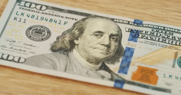 Gros plan sur le billet de 100 dollars avec Franklin sur le billet. Fond de bureau en bois. Macro — Video