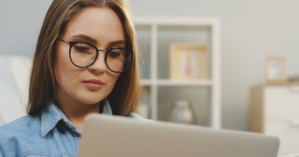 Porträtt skott av allvarliga unga kvinnan i glasögon som arbetar på den bärbara datorn hemma i vardagsrummet. Närbild — Stockvideo