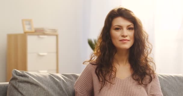 Close up van de aantrekkelijke jonge vrouw met krullend haar draaien haar hoofd en het glimlachen naar de camera in de gezellige woonkamer. Binnenkant. Portret — Stockvideo