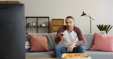 Oturma odasında kalan sahip, gri kanepede oturan ve pizza yemek yakışıklı delikanlı. Evde. İçinde