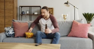 Cips yiyip bira içmeyi spor oyun, izlerken beyaz iyi görünümlü bir adam. Gergin olma. Evde. Kapalı