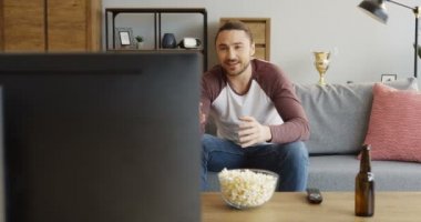Televizyon karşısında kanepede patlamış mısır ve bira ile spor oyunu ve onun takım kaybetme izlerken oturan genç iyi görünümlü adam portre vurdu. Kapalı