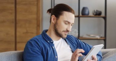 Rahat oda içinde kanepede oturan sonra bir kafa dönme ve gülümseyen bir tablet bilgisayar kullanma yakışıklı beyaz adamın kapatın. İçinde