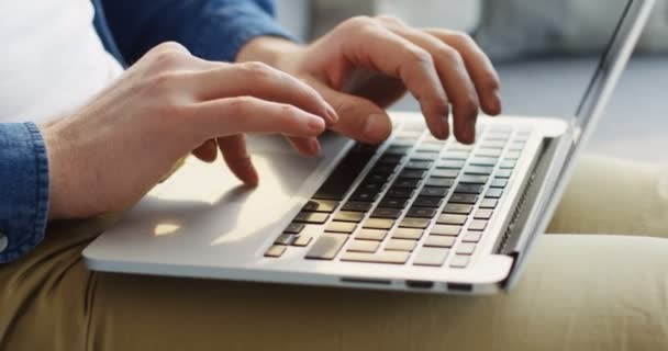 Primer plano de las manos caucásicas masculinas trabajando en el ordenador portátil mientras lo sostiene de rodillas. Trabajar en casa . — Vídeos de Stock