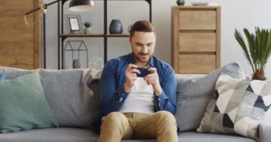 Rahat oda içinde kanepede oturan ve Smartphone, o zaman kızgın çünkü kaybedilen oyun casual tarzda beyaz adam heyecanlı. Evde. İçinde