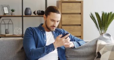 Çekici genç bir kuyruk oturma odasında kanepede oturan ve Smartphone'da taping kot gömlek. İçinde