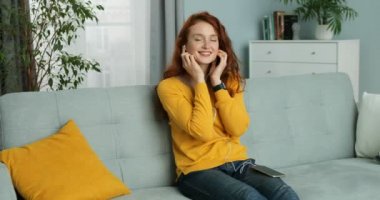 Kızıl saçlı, beyaz, sarı kazaklı ve kulaklıklı güzel, neşeli bir kadın evdeki kanepede oturuyor. Güzel kız akıllı telefondan müzik dinliyor, şarkı söylüyor ve gülümsüyor. Kadın şarkıdan zevk alıyor..