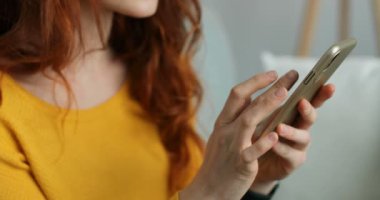 Kafkasyalı kızıl kıvırcık saçlı kadının ellerinde akıllı telefonu kapat. Kadın telefon dinlemesi ve kaydırma yapıyor. - Evde. Kapalı alanda. Cep telefonundan mesaj atan bir kız. İnternette sohbet..