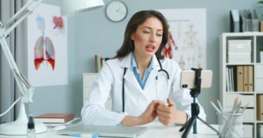 Kafkasyalı genç bayan doktor, hastayla çevrimiçi video kaset aracılığıyla konuşuyor. Kabinede akıllı telefondan ve danışmanlık yaparak. İnternette internet kamerasından danışmanlık yapan bir kadın doktor. Video sohbet konsepti.