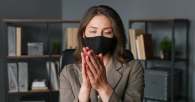 Maskeli güzel beyaz iş kadını masada oturuyor ve elinde dezenfektan püskürtüyor. Coronavirus salgını koruması. Kadın temizliği, sterilize etme ve mikroplardan deriyi temizleme..
