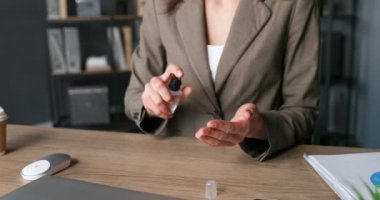 Kadın ellerine yakın çekim. Beyaz kadın masada oturuyor ve cildine dezenfektan püskürtüyor. Coronavirus salgını koruması. Kadın temizleme, sterilize etme ve parmakları sterilize etme.