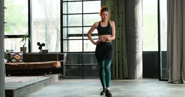 Jeune femme sportive caucasienne debout dans le salon et réchauffant ses jambes. Femme entraînant son corps à s'isoler en quarantaine. Jolie fille de formation et de travail à la maison . — Video