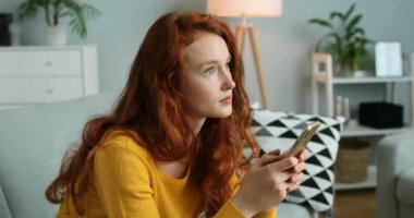 Güzel, beyaz saçlı, kıvırcık saçlı, akıllı telefondan mesaj atan ve oturma odasındaki kanepede gülümseyerek düşünen güzel bir kadın. Güzel bir kız cep telefonunu dinleyip kaydırıyor. Evde..