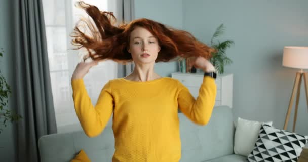 Retrato de una joven caucásica pelirroja sonriendo en una acogedora sala de estar. Hermosa chica elegante con el pelo rizado rojo mirando a la cámara como en el espejo. En el interior. En casa. . — Vídeos de Stock