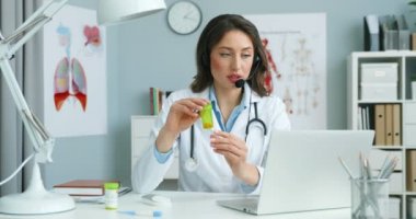 Kafkas kadın doktor hastayla çevrimiçi video kaset aracılığıyla konuşuyor ve dolaptaki dizüstü bilgisayarda hapları gösteriyor. Kadın doktor internette danışmanlık yapıyor ve tıp hakkında danışmanlık yapıyor..
