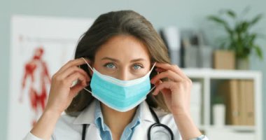 Mavi tıbbi maske takan ve dolaptaki kameraya bakan beyaz, güzel kadın doktorlara yakın durun. Koronavirüsten korunan güzel bir kadın doktorun portresi..