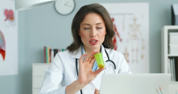 Kobieta lekarz rozmawia z pacjentem online videochat na laptopie i pokazując pigułki. Kobieta medyk po konsultacji w Internecie na komputerze przez kamerę internetową. Wykazanie się środkami zaradczymi. Konsultacje medyczne — Wideo stockowe