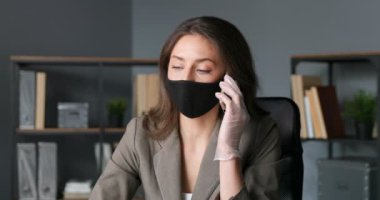 Kafkasyalı genç iş kadını cep telefonuyla konuşuyor. Maskeli güzel bayan ofis çalışanı dolapta cep telefonuyla konuşuyor. Coronavirus salgını zamanı. Telefon eden bir kadın..