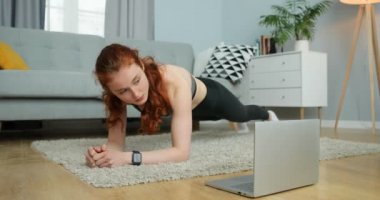 Kafkasyalı genç kızıl saçlı kadın evde kendini izole ederek çalışıyor. Güzel bir kız dizüstü bilgisayarın önünde çevrimiçi antrenörle birlikte duruyor. Karantina eğitimi.