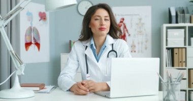 Beyaz cüppeli beyaz bir kadın doktorun, rahat dolabında oturmuş kameraya bakarken çekilmiş portresi. Laptop bilgisayarında çekici bayan doktor.