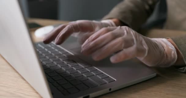 Närbild av kaukasiska kvinnliga händer i gummihandskar skriva och knacka på tangentbord bärbar dator på kontoret på skrivbordet. Träbord. Begreppet skydd mot pandemisk Coronavirus. — Stockvideo